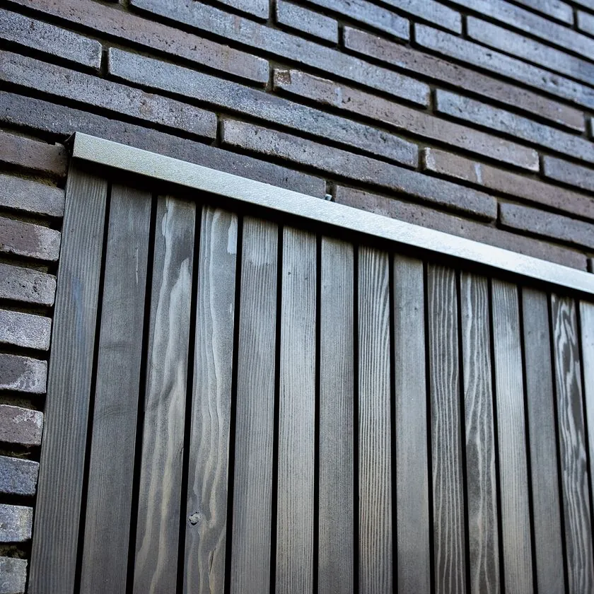 Detail of black linear brick meeting dark vertical timber boarding with a metal capping