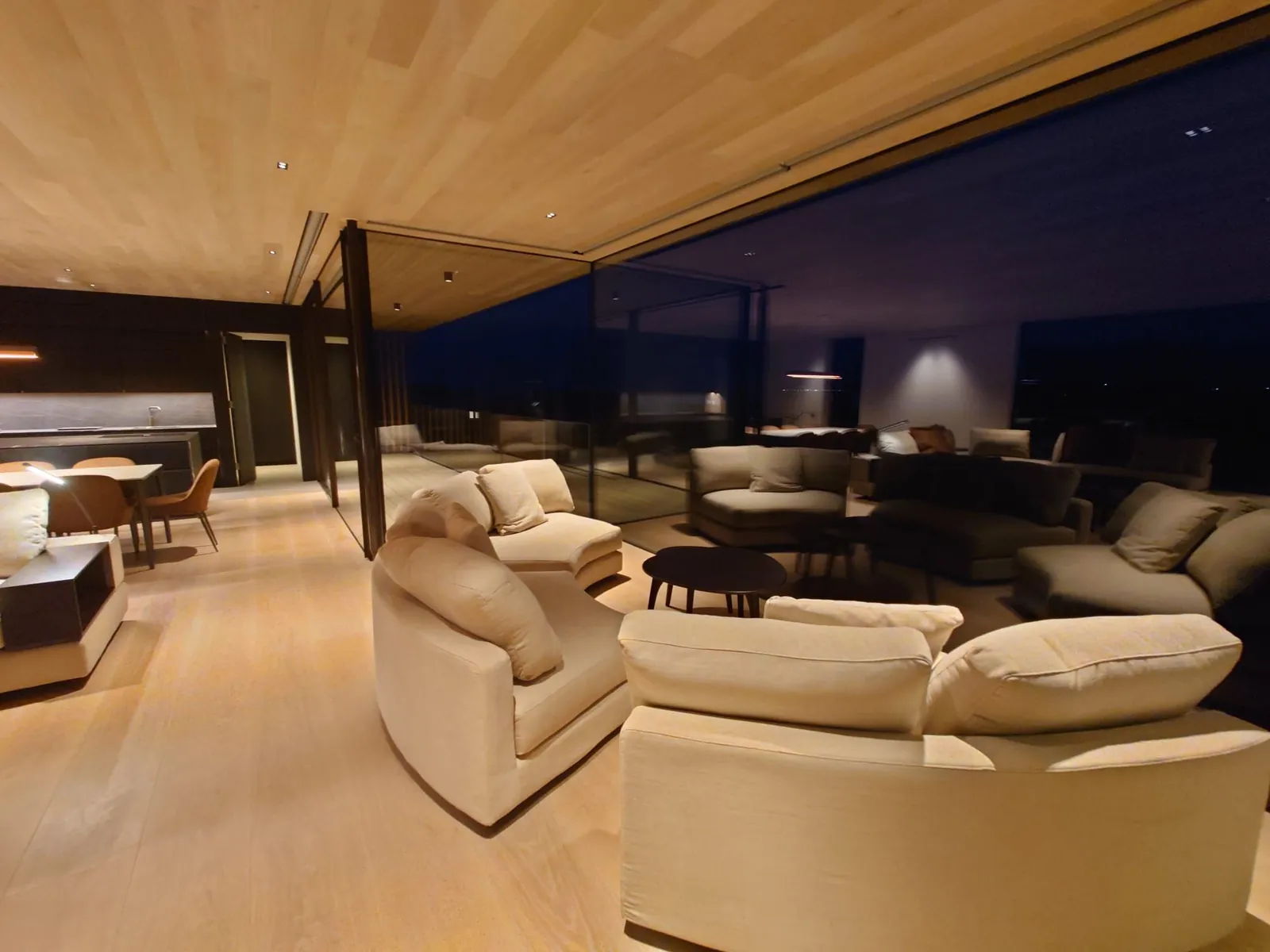 Open-plan living space in the evening, under a timber-lined ceiling