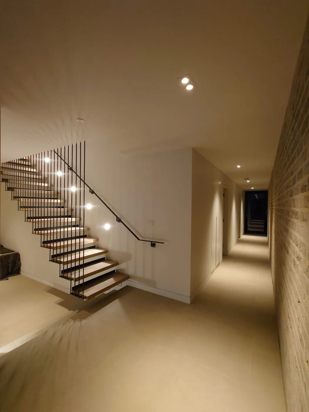 Cantilevered stair with lit treads rising beside a long hallway